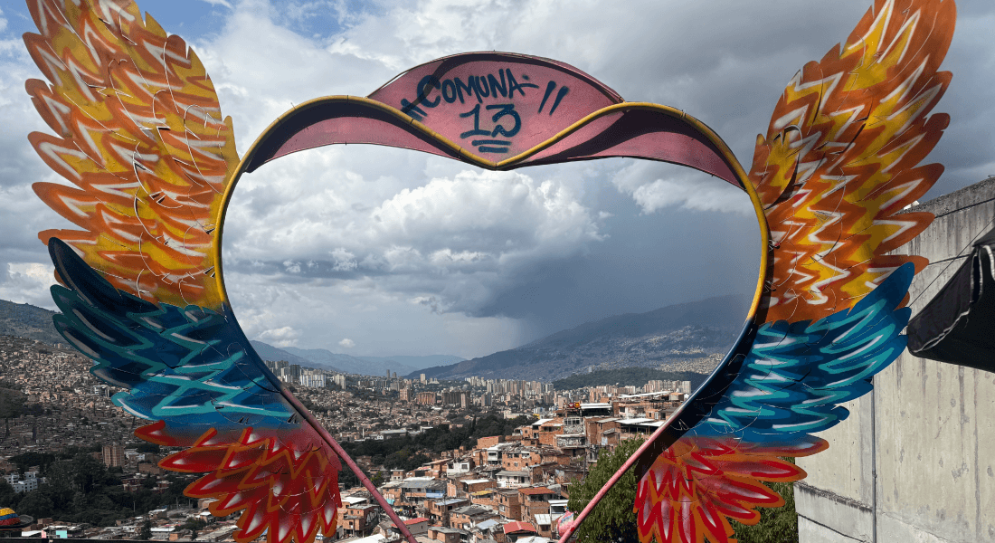A heart-with-wings sculpture frames a city skyline in the background.