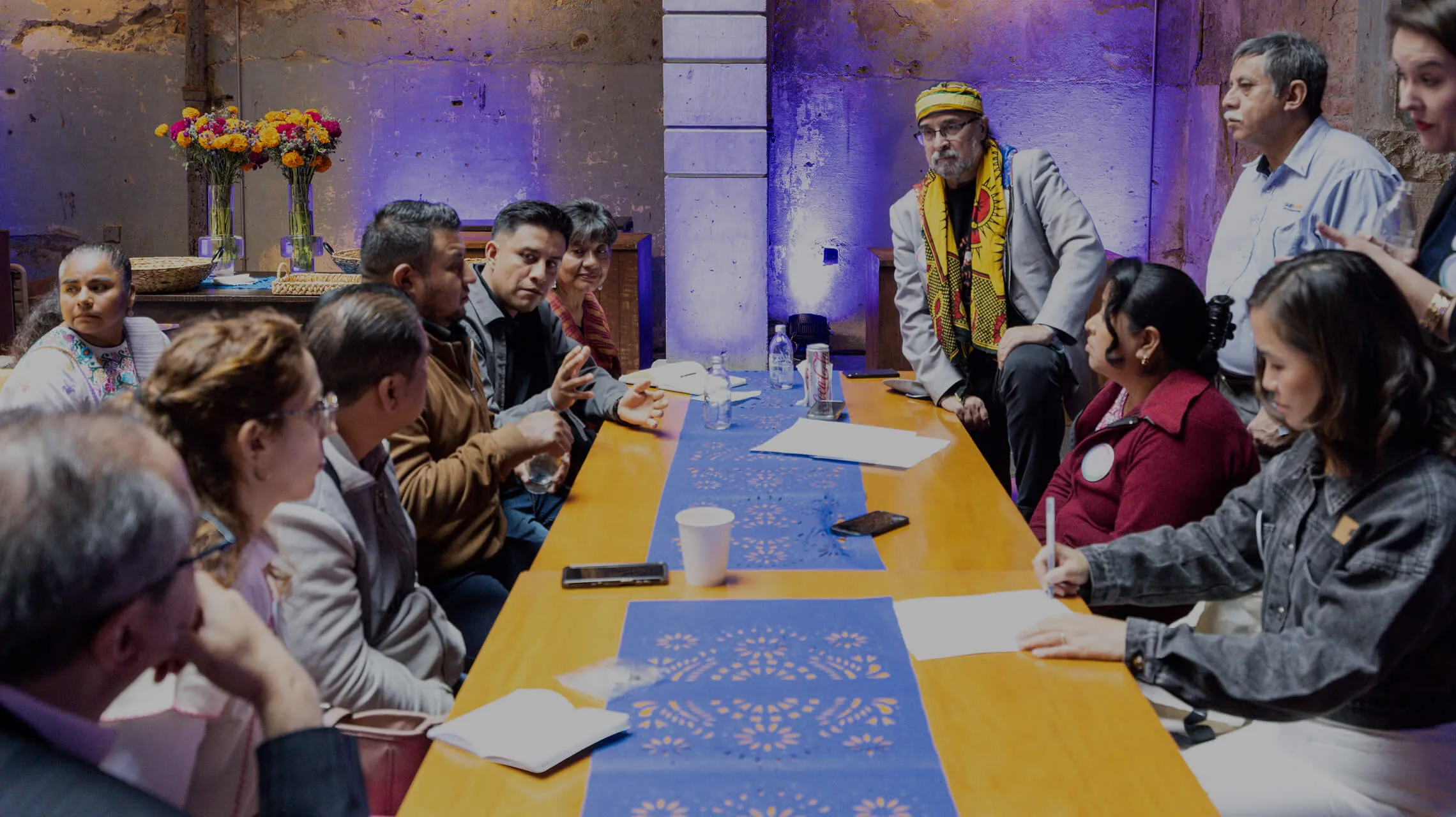 People seated around a long table during a community workshop, talking and taking notes