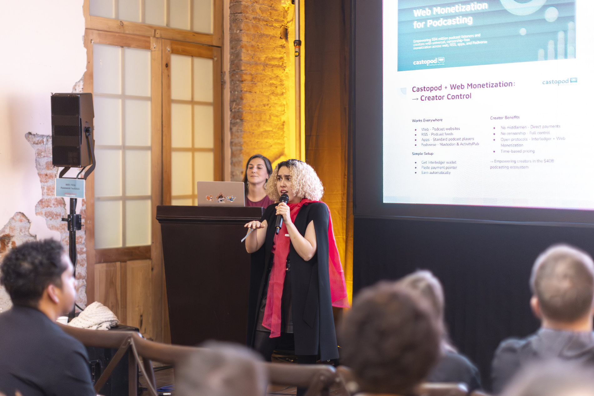 A speaker presenting Web Monetization for podcasting on stage, with a Castopod slide behind her and an audience in the foreground.